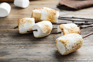 Photo of Twigs with roasted marshmallows on wooden table, closeup