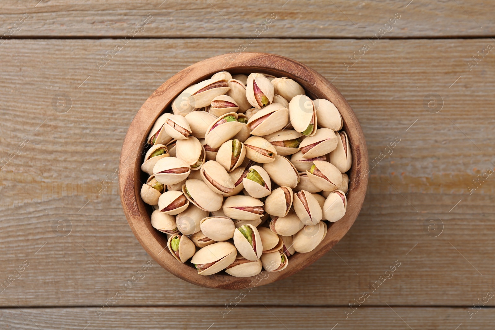 Photo of Tasty pistachios in bowl on wooden table, top view