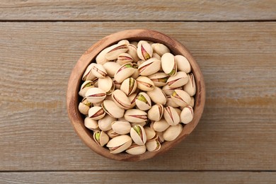 Tasty pistachios in bowl on wooden table, top view