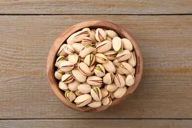 Photo of Tasty pistachios in bowl on wooden table, top view