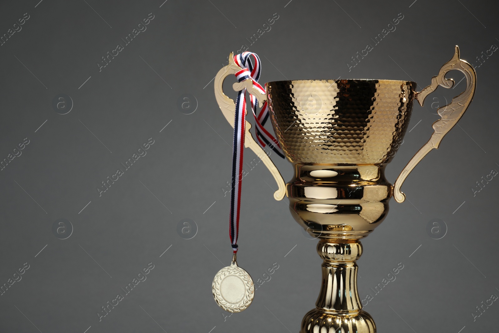 Photo of Golden trophy cup and medal on grey background. Space for text