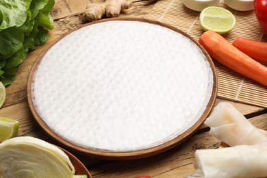 Photo of Making delicious spring rolls. Rice paper and other ingredients on wooden table, closeup