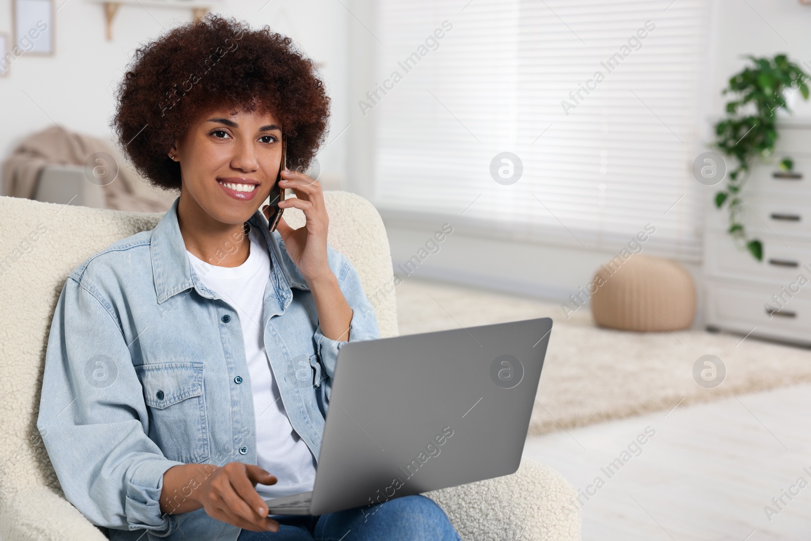 Photo of Young woman using laptop and talking on smartphone in room, space for text
