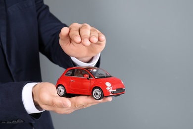 Photo of Male insurance agent holding toy car on grey background, closeup. Space for text