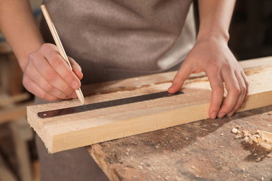 Professional carpenter measuring wooden plank in workshop, closeup
