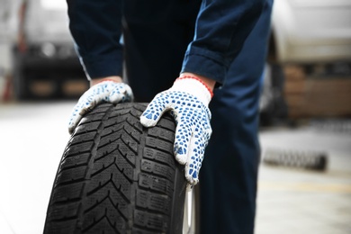 Mechanic with car tire in service center, closeup
