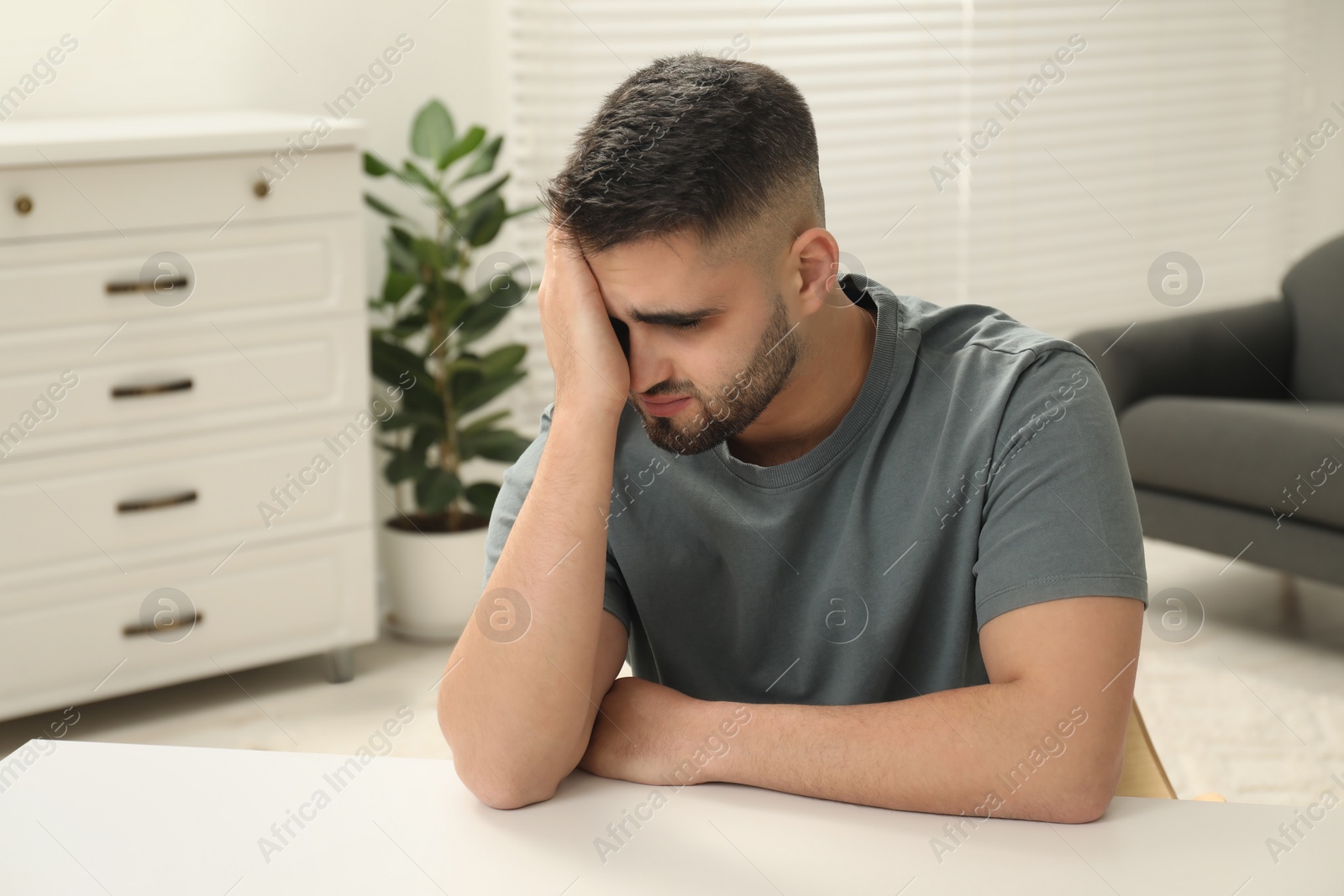 Photo of Sad man sitting at white table indoors