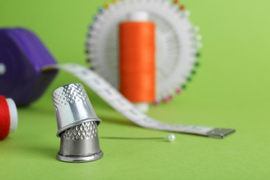 Photo of Thimbles and different sewing tools on green background, closeup. Space for text