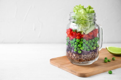 Photo of Healthy salad in glass jar on white wooden table. Space for text