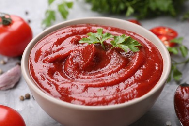 Organic ketchup and parsley in bowl on grey table, closeup. Tomato sauce