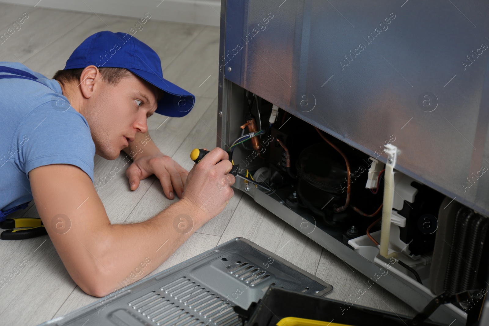 Photo of Male technician with screwdriver repairing refrigerator indoors