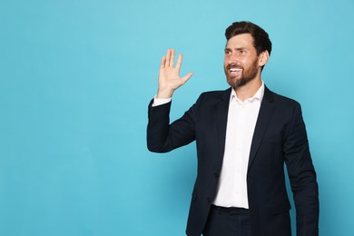 Photo of Smiling bearded man in suit showing hand on light blue background. Space for text