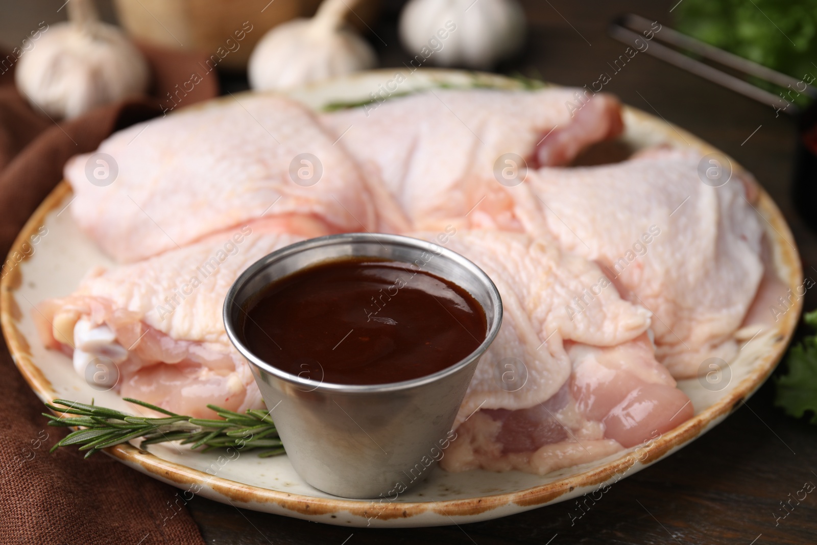 Photo of Plate with fresh marinade, raw chicken and rosemary on wooden table, closeup