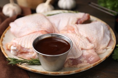 Plate with fresh marinade, raw chicken and rosemary on wooden table, closeup