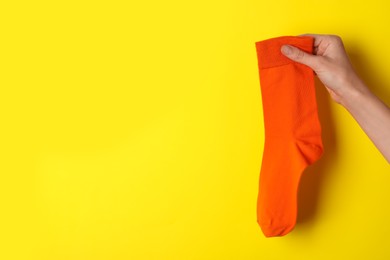 Photo of Woman holding orange sock on yellow background, closeup. Space for text