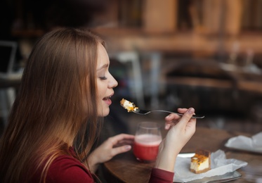 Photo of Pretty young woman with cocktail and cake at table in cafe, view from outdoors through window