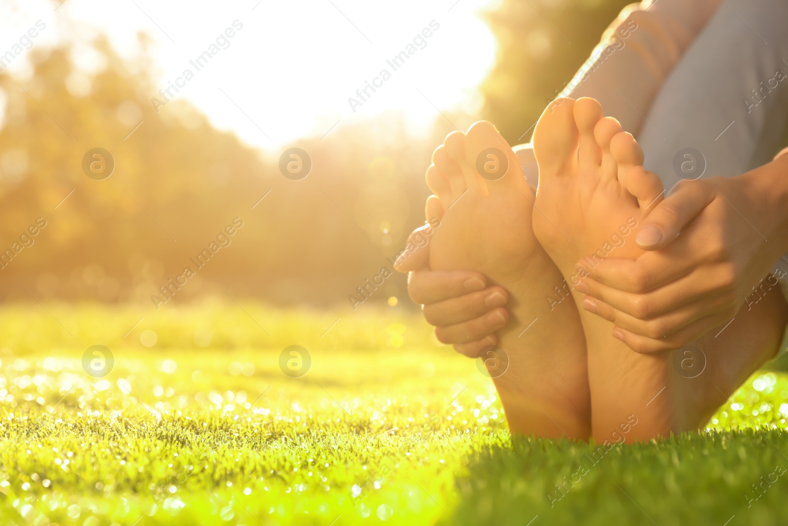 Photo of Young woman sitting barefoot on fresh green grass outdoors, closeup