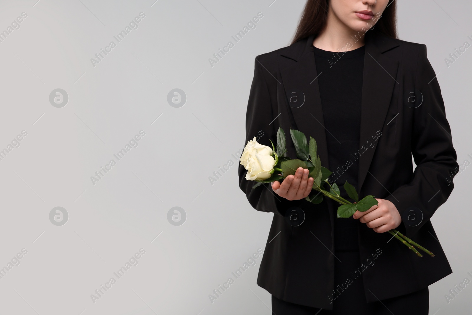 Photo of Woman with white rose flowers on light grey background, closeup and space for text. Funeral ceremony