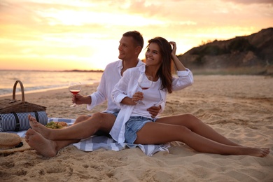 Photo of Lovely couple having romantic picnic on beach at sunset