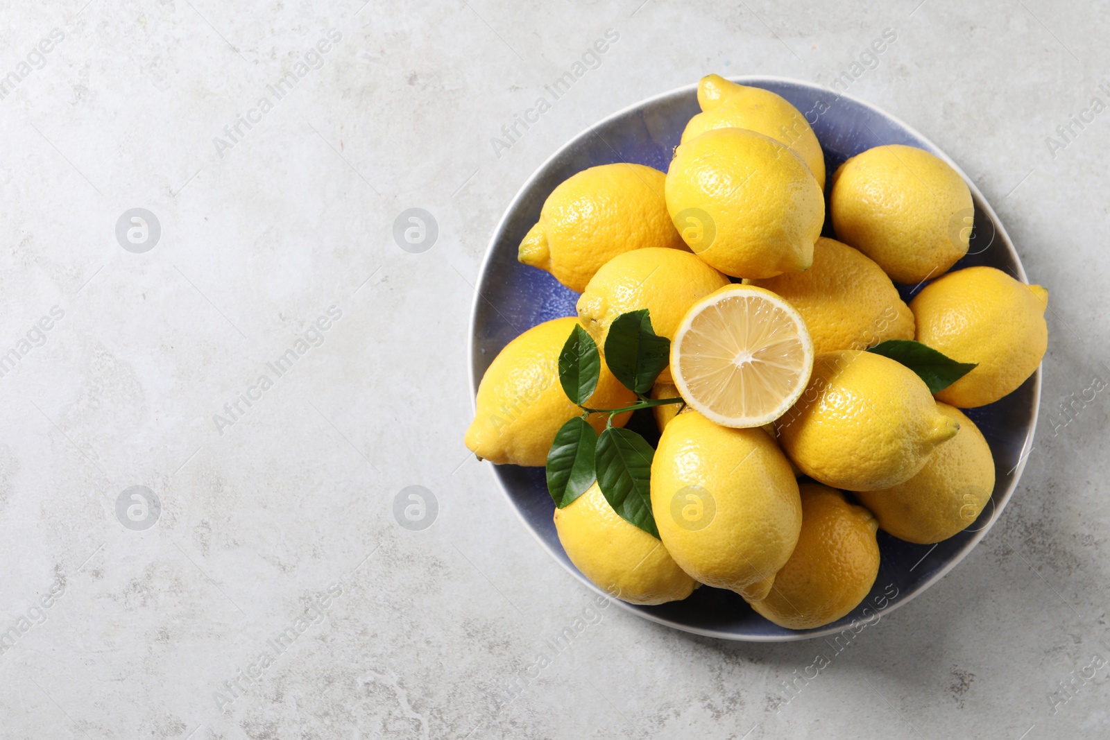 Photo of Fresh lemons and green leaves on light table, top view. Space for text