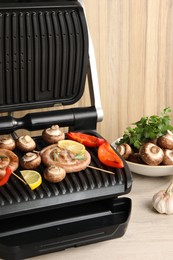 Photo of Electric grill with homemade sausages, mushrooms and bell pepper on wooden table