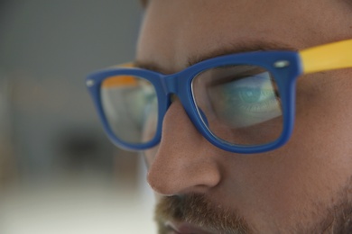 Photo of Young man wearing glasses on blurred background, closeup. Ophthalmology service