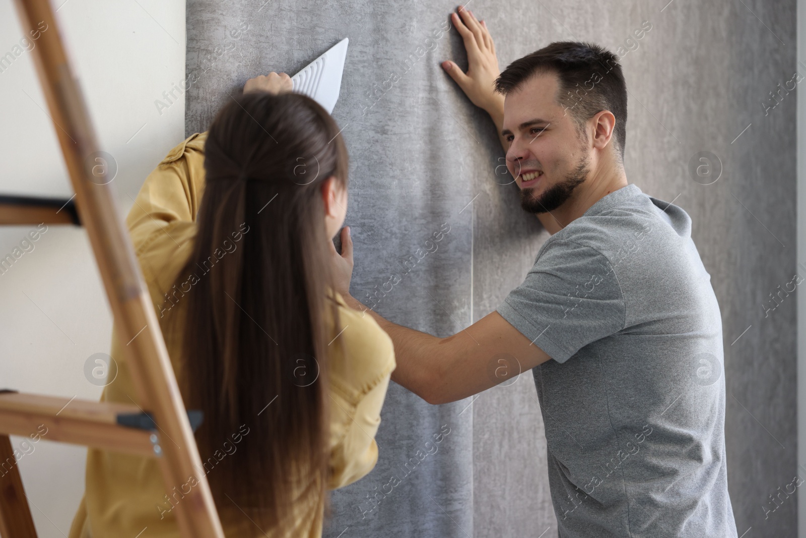 Photo of Couple hanging stylish gray wallpaper in room