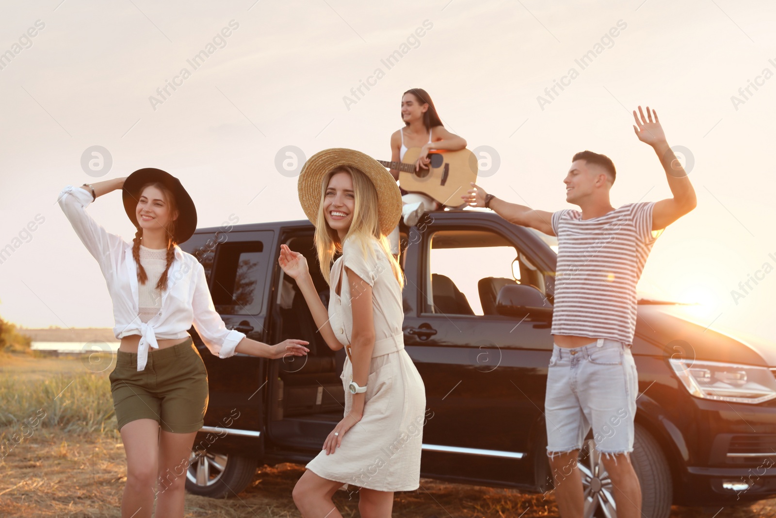 Photo of Happy friends having fun near car outdoors at sunset. Summer trip