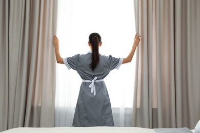 Chambermaid opening curtains in room. Hotel service