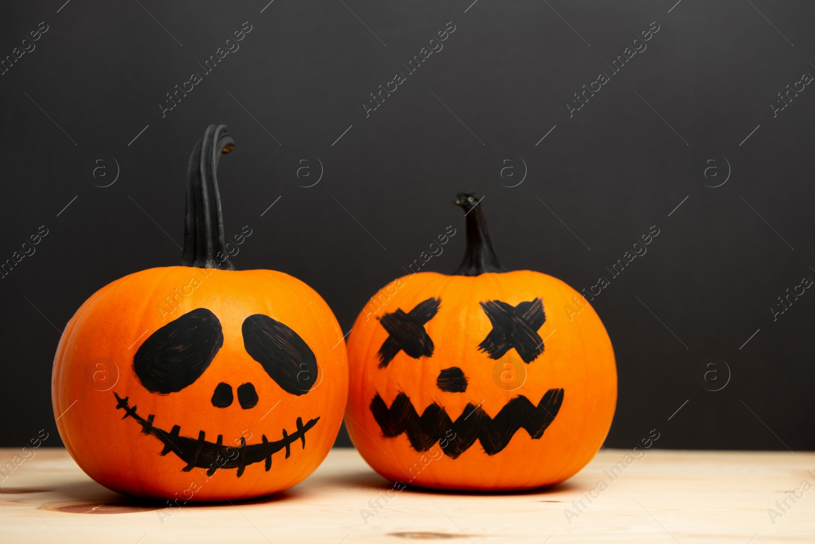 Photo of Halloween pumpkins with drawn faces on wooden table against dark background, space for text
