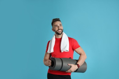 Beautiful man with yoga mat and towel on turquoise background