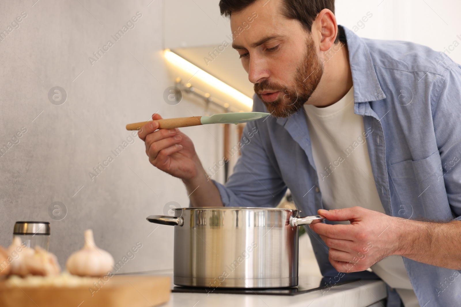 Photo of Man tasting delicious chicken soup in kitchen