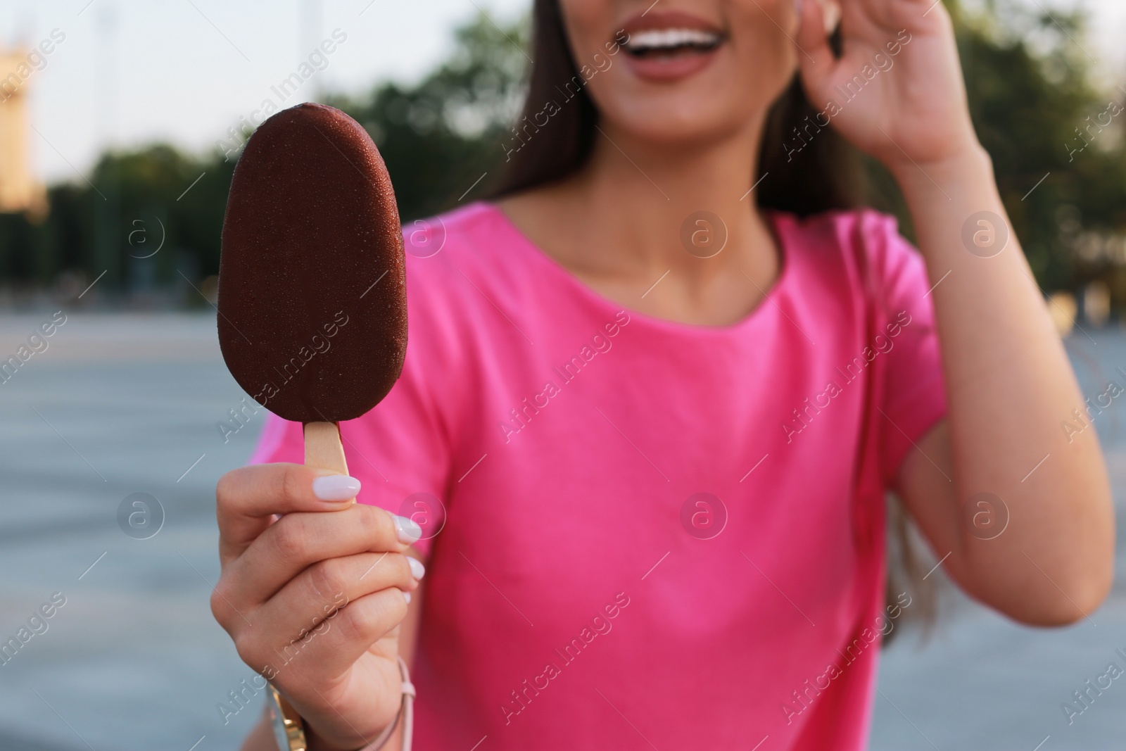 Photo of Young woman holding ice cream glazed in chocolate on city street, closeup