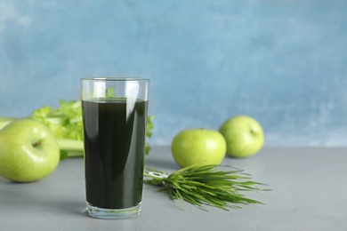 Photo of Glass of spirulina drink, wheat grass and apples on table against color background. Space for text