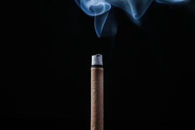 Photo of Incense stick smoldering on black background, closeup