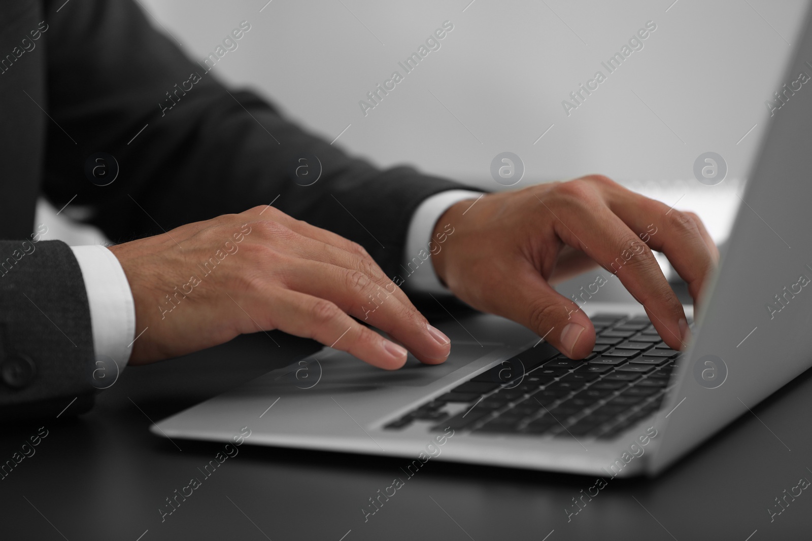 Photo of Man using modern laptop at black desk, closeup