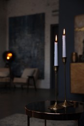 Pair of beautiful candlesticks on glass table in room, space for text