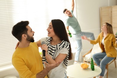 Photo of Happy couple singing karaoke with friends at home