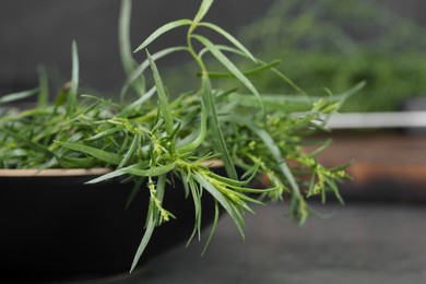 Photo of Fresh tarragon sprigs in bowl on table, closeup. Space for text