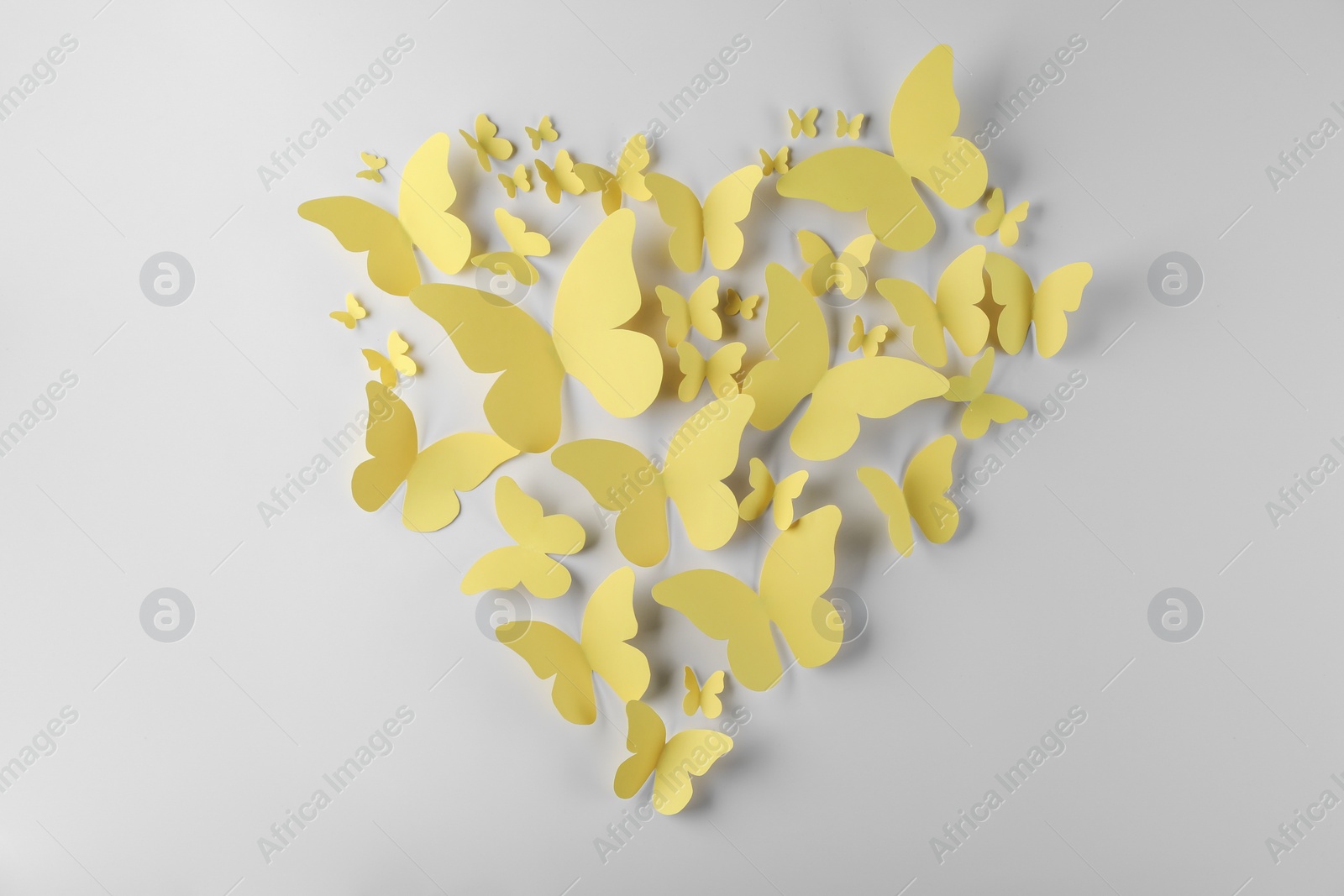 Photo of Heart shape made of yellow paper butterflies on white background, top view