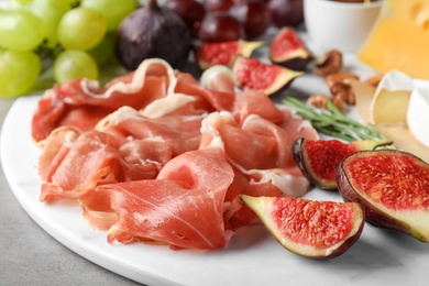 Delicious ripe figs and prosciutto served on grey table, closeup