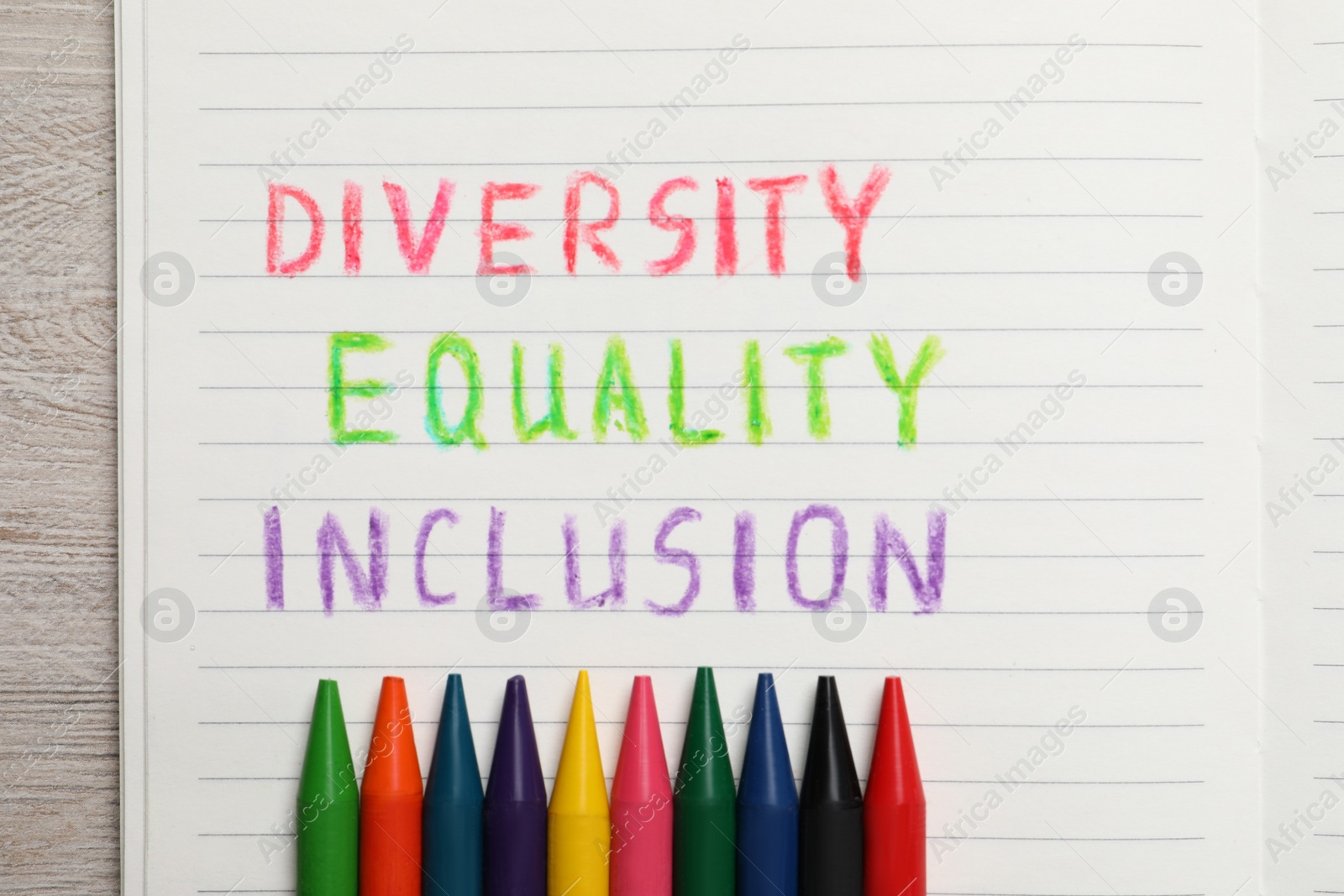 Photo of Notebook with words Diversity, Equality, Inclusion and wax pencils on wooden table, top view