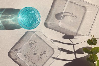 Photo of Jar and samples of transparent cosmetic gel on light table, flat lay