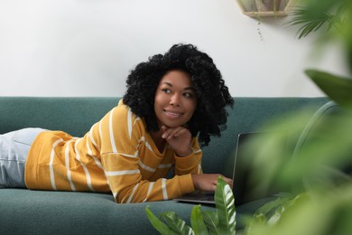 Relaxing atmosphere. Woman with laptop lying on sofa near houseplants indoors