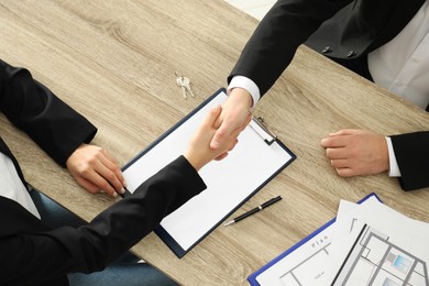 Photo of Real estate agent shaking hands with client at table in office, above view