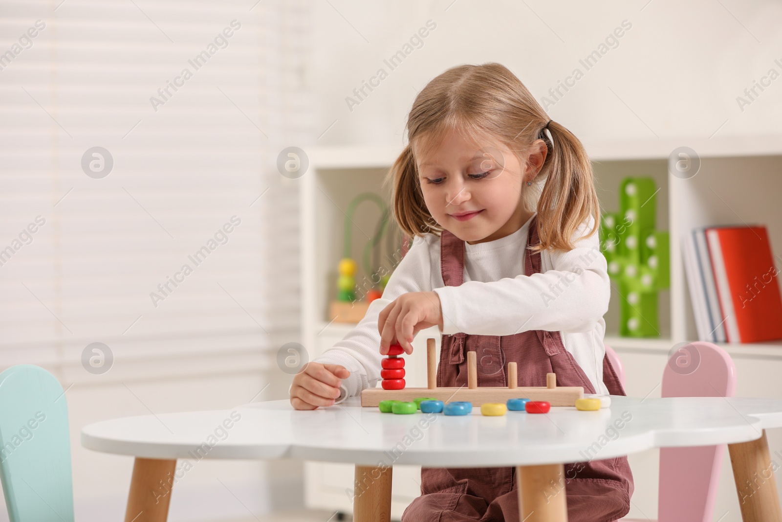 Photo of Cute little girl playing with stacking and counting game at white table indoors, space for text. Child's toy