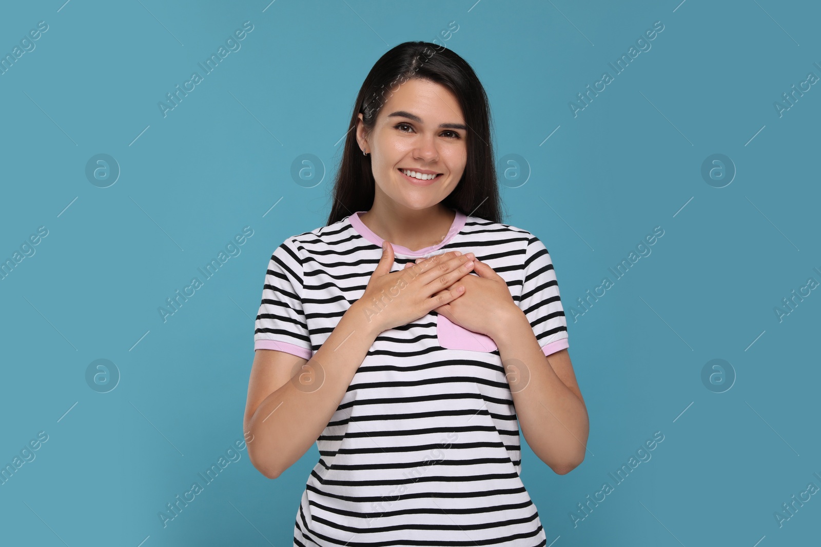 Photo of Thank you gesture. Beautiful grateful woman holding hands near heart on light blue background