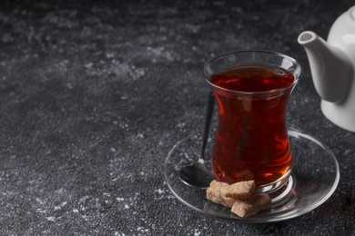 Photo of Glass of traditional Turkish tea and sugar on grey textured table, closeup. Space for text
