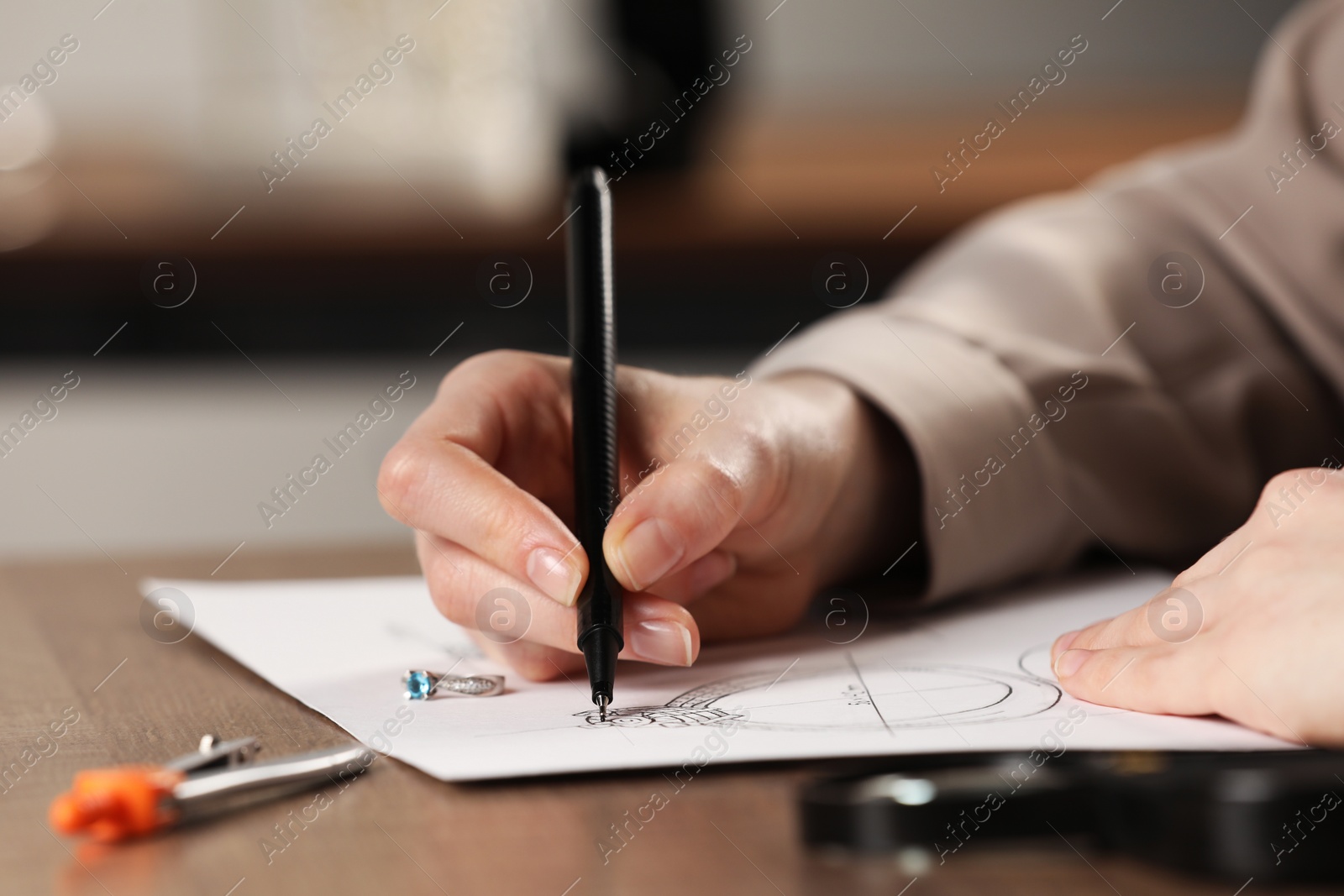 Photo of Jeweler drawing sketch of elegant ring on paper at wooden table indoors, closeup