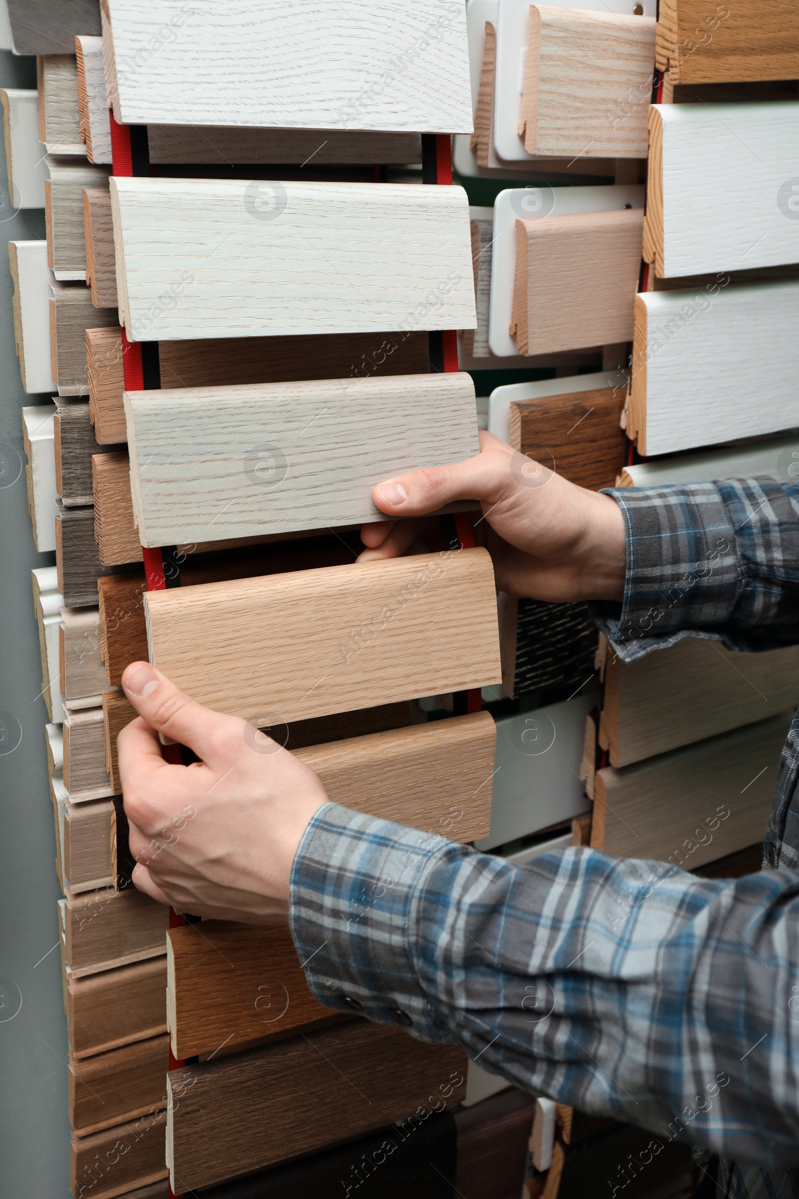 Photo of Man choosing wooden flooring among different samples in shop, closeup